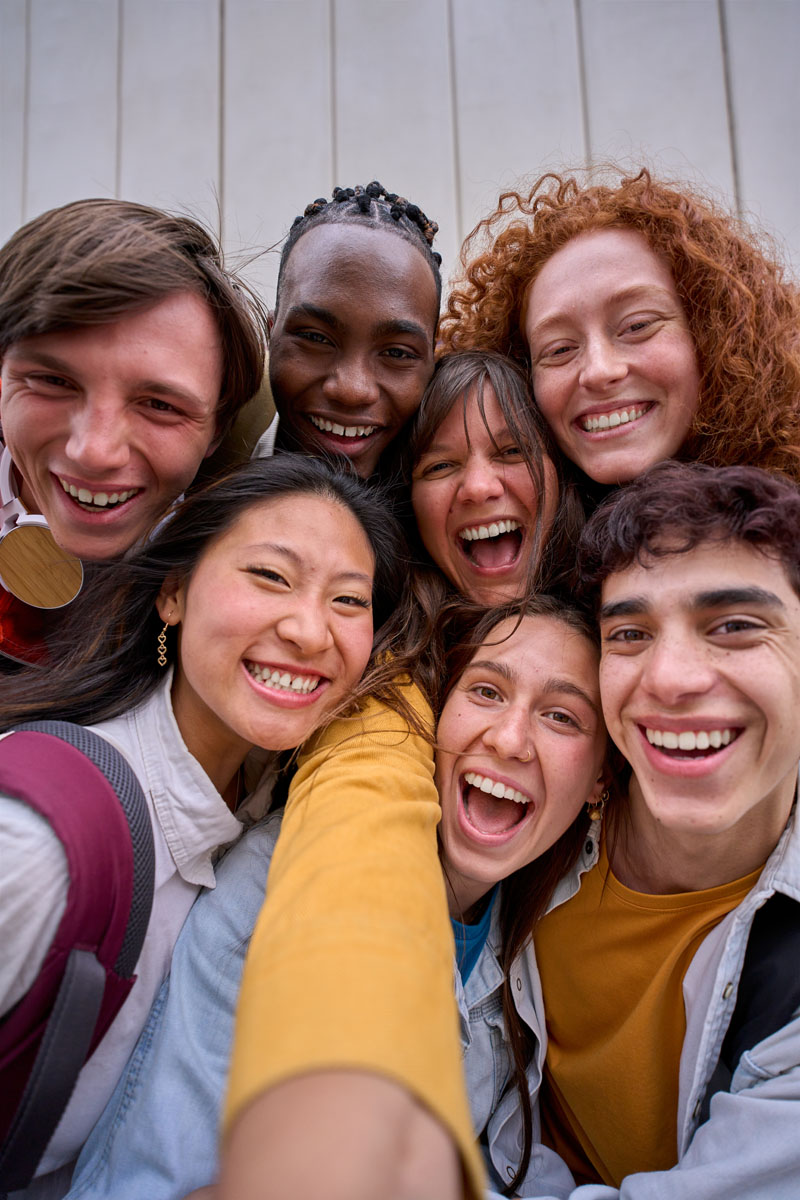 Vertical phone selfie of excited multiracial group of erasmus college students together outside. Vertical cell phone selfie of excited multiracial group of erasmus college students together outside. Cheerful smiling young friends pose laughing for photo. Happy people on campus.
